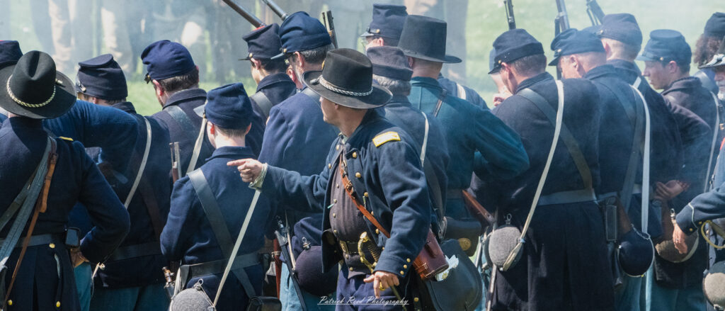 A Union officer directing their troops, gesturing with authority as they provide instructions. Dressed in a distinctive blue uniform, the officer's expression is determined and focused, showcasing leadership and the responsibility of guiding soldiers during a critical moment in battle.